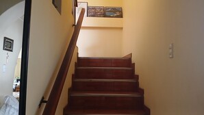 Una escalera con barandillas de madera y un pared lisa con algunas fotografías enmarcadas.
