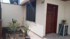 Una entrada de casa con puerta de madera, ventana con rejas y plantas en macetas.