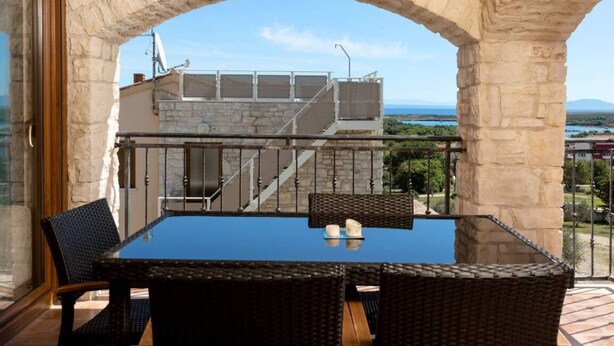 A balcony with a glass table and wicker chairs, overlooking a staircase and a scenic view. - Apartman R&G Serenity (Ližnjan)