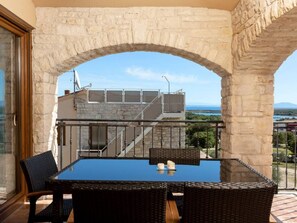 Een balkon met een glazen tafel en rieten stoelen, met uitzicht op een trap en een prachtig landschap.