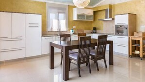 A modern kitchen with white cabinets, a wooden dining table, and a hanging light fixture. - Apartman R&G Serenity (Ližnjan)