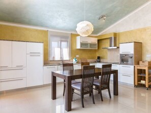 A modern kitchen with white cabinets, a wooden dining table, and a hanging light fixture. - Apartman R&G Serenity (Ližnjan)