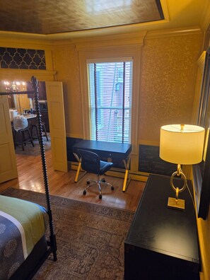 A hotel room with a bed, a desk, a chair, a lamp, and a window with blinds.