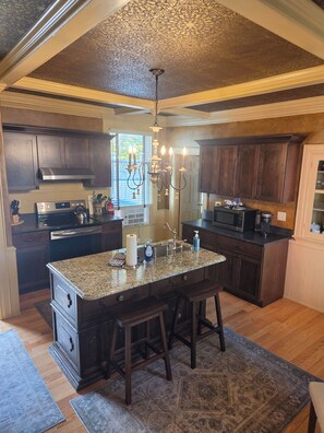 A kitchen with dark wood cabinets, a granite countertop island, stainless steel appliances, and a patterned ceiling.