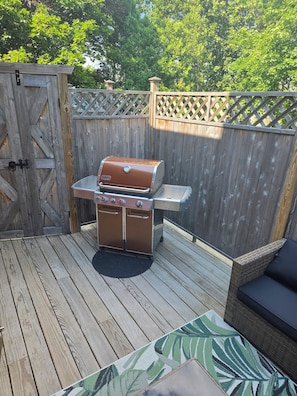 A wooden deck with a barbecue grill, a wicker sofa, and a lattice fence.