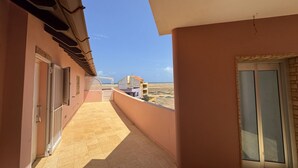 Un couloir au sol carrelé mène à un balcon d’où l’on peut admirer la plage et les autres bâtiments.