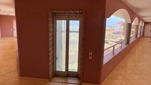 Un couloir avec une porte en verre donnant sur un balcon d’où l’on peut admirer les bâtiments et un ciel dégagé.