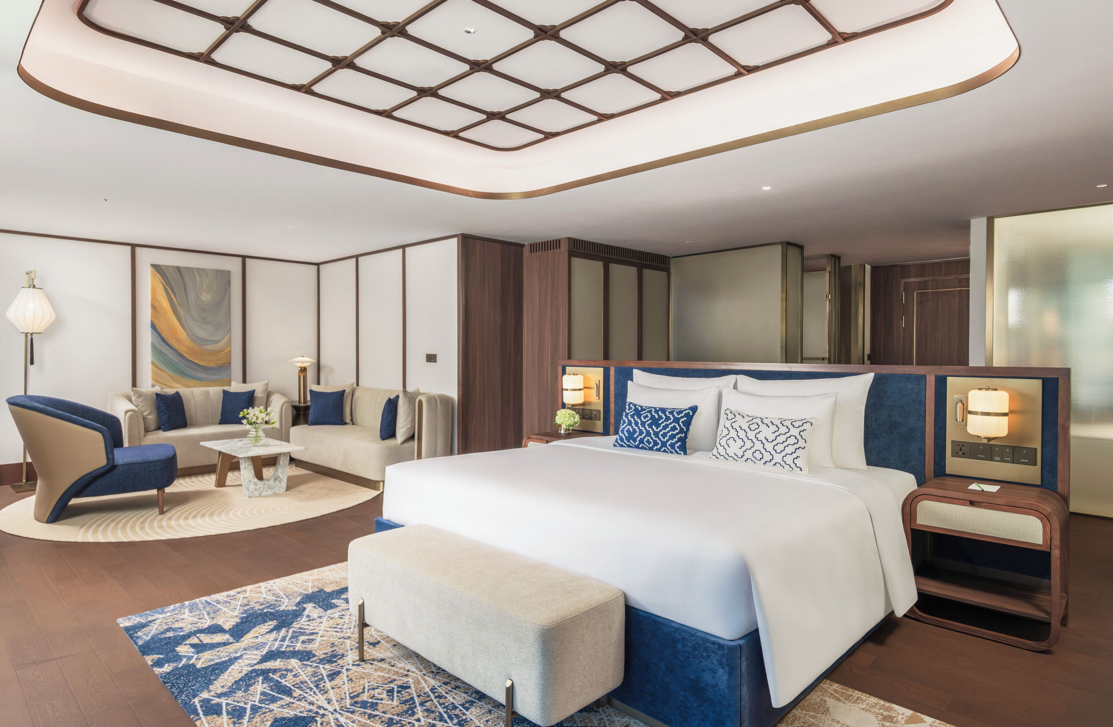 Une chambre d’hôtel moderne dotée d’un grand lit, d’un coin salon avec un canapé et un fauteuil, d’une petite table et d’un tapis décoratif.