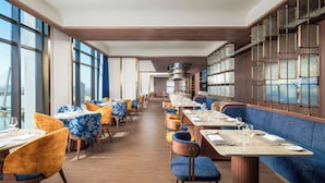 A restaurant with a long counter, blue and yellow upholstered chairs, and large windows. - TUI BLUE Han River (Da Nang)