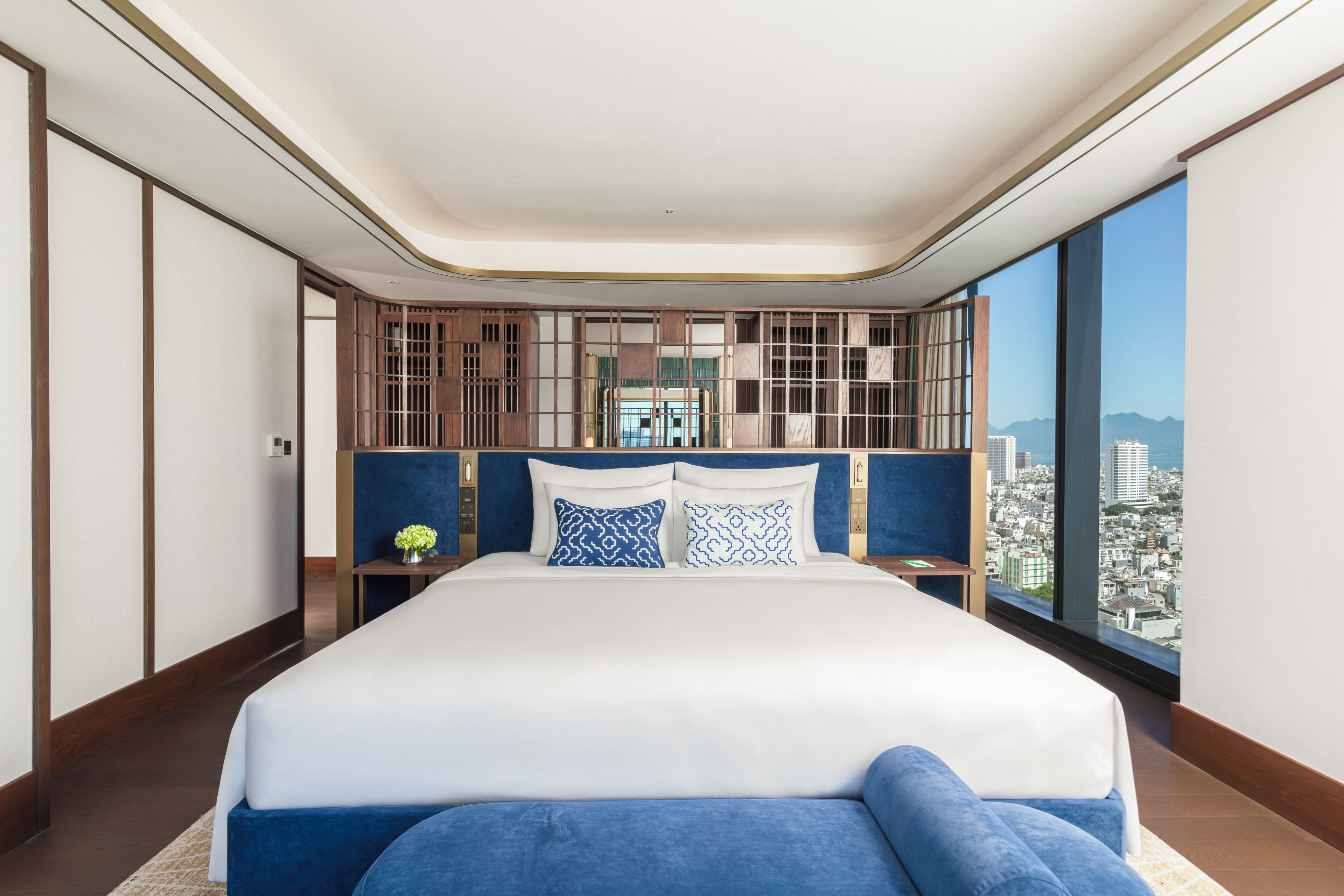 A modern hotel room with a large bed, a view of the city, and a unique wooden partition.