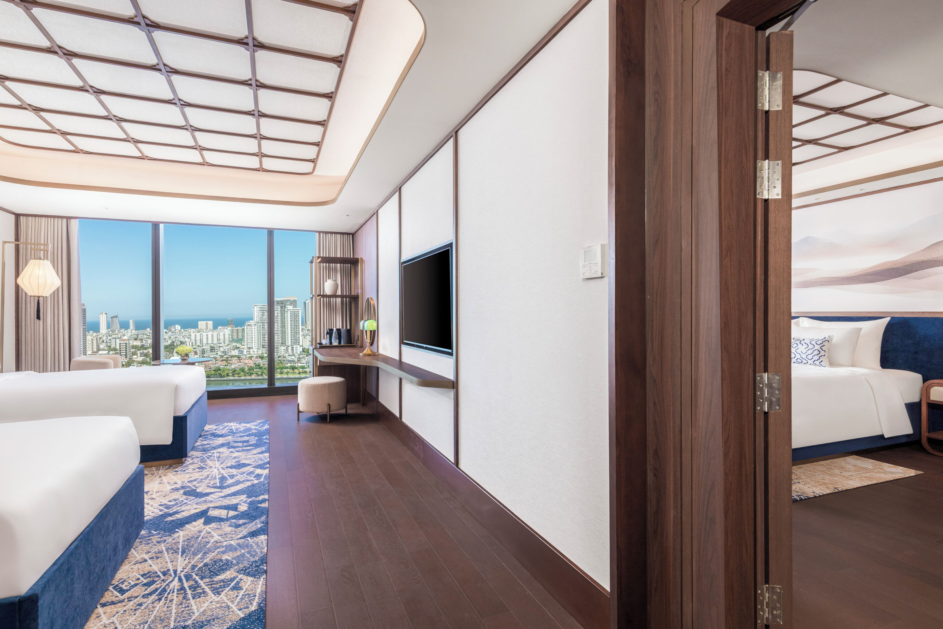 A hotel room with a city view, a large bed, a smaller bed, a TV, and a desk.