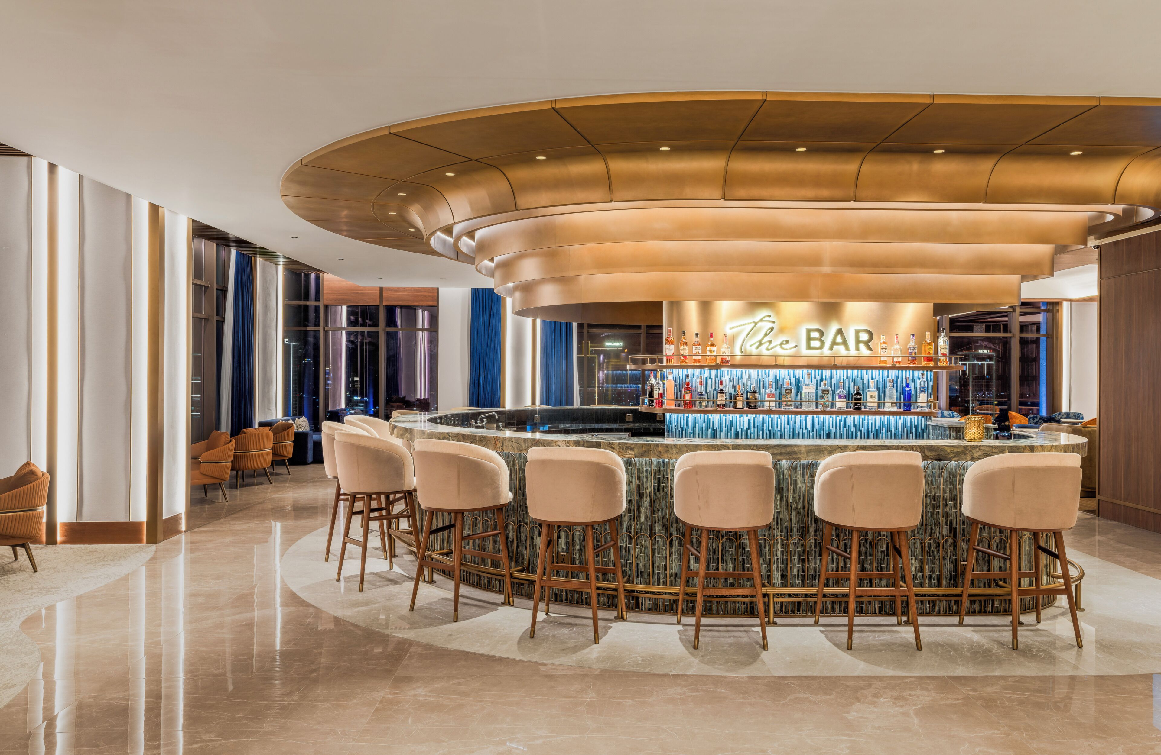 Zona de bar moderna con techo curvo, taburetes y una variedad de botellas.