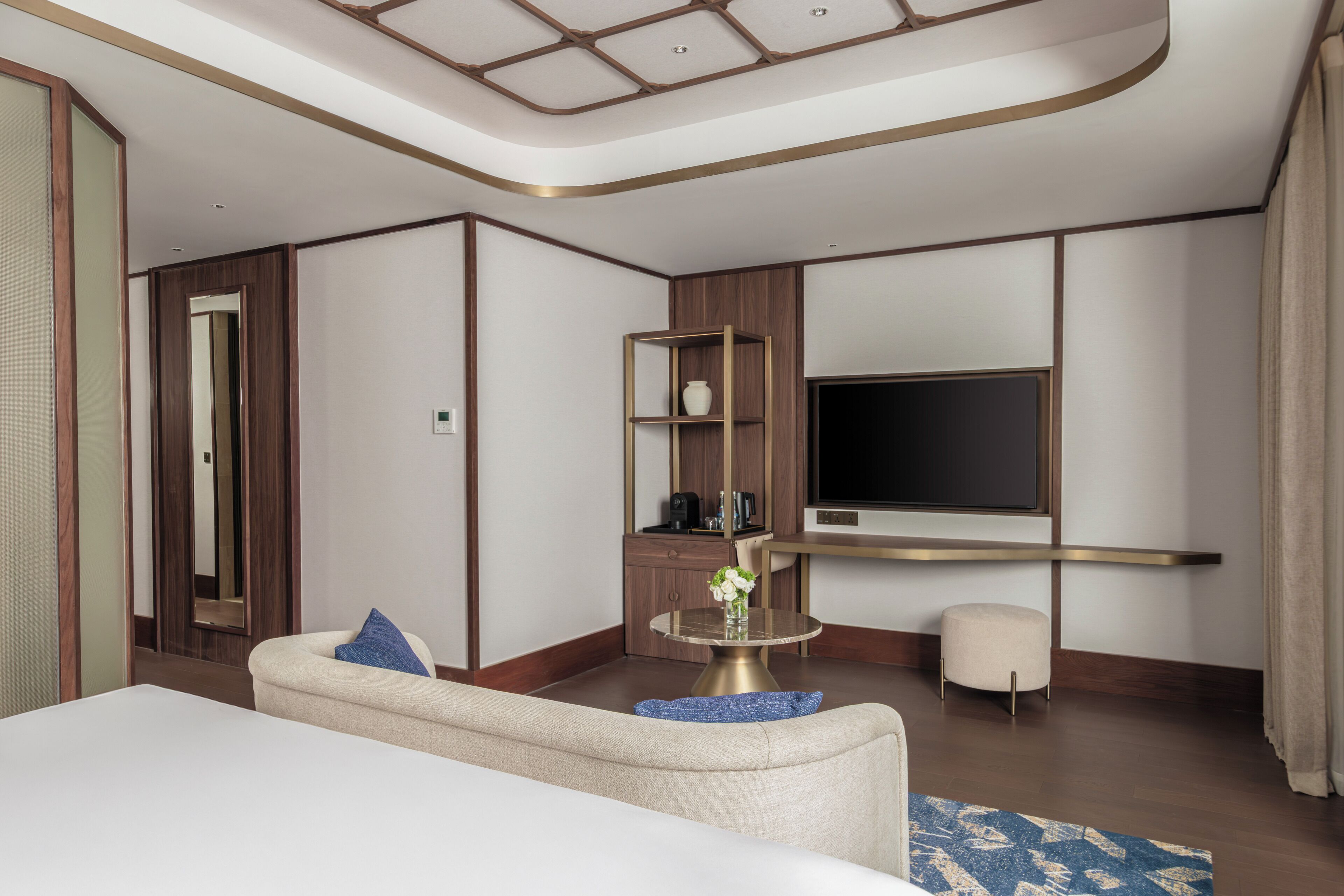 Una moderna camera d'albergo con un letto grande, un'area salotto, una televisione appesa al muro e un piccolo tavolino.