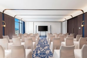 A conference room with rows of white chairs, a large screen, and a patterned carpet. - TUI BLUE Han River (Da Nang)