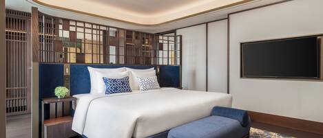 A modern bedroom with a large bed, a TV mounted on the wall, and a decorative partition.