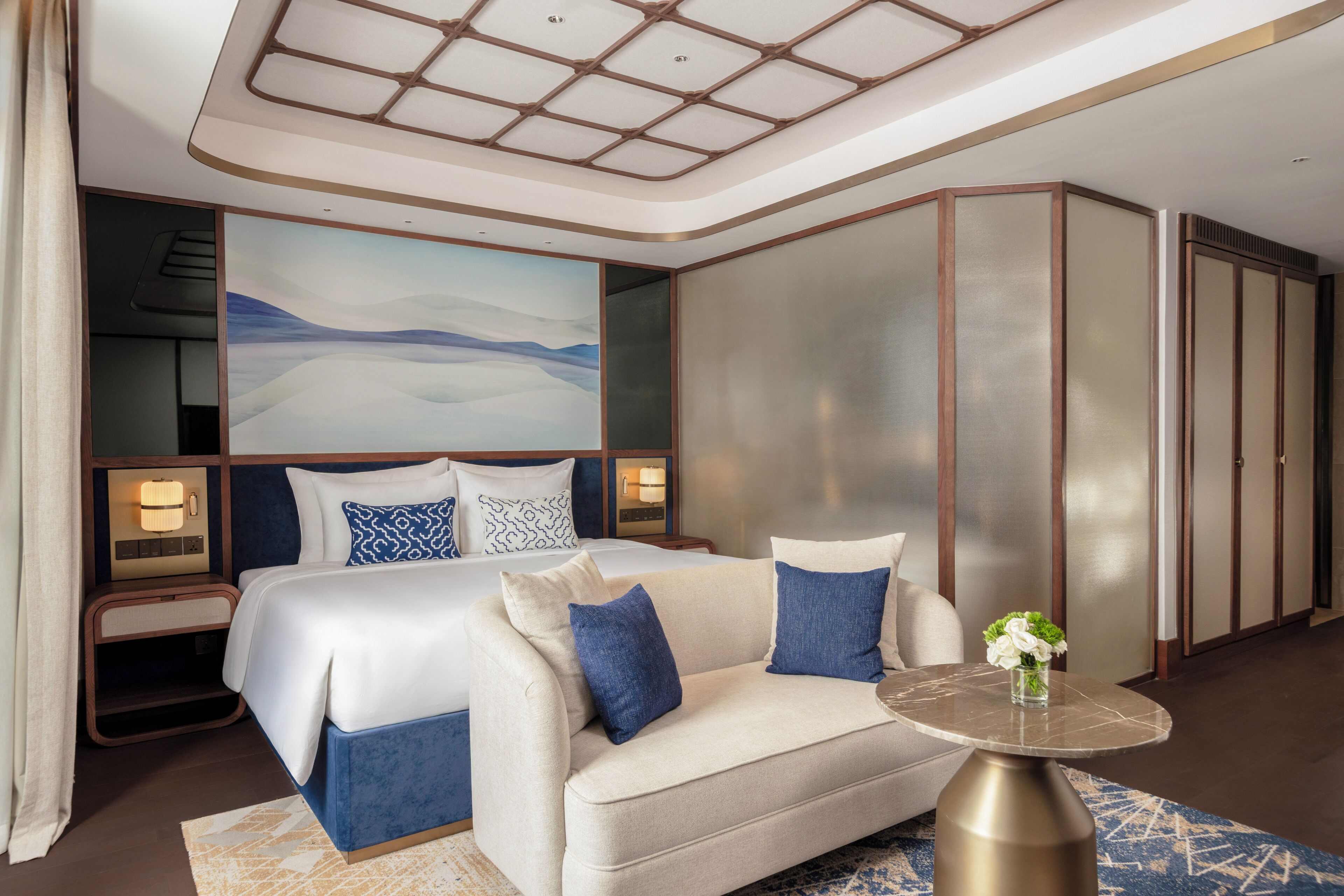 A hotel room with a large bed, a sofa, a small table, and a large painting on the wall.