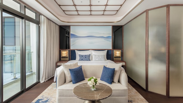 A modern hotel room with a large bed, a sofa, a round table, and a cityscape view. - TUI BLUE Han River (Da Nang)
