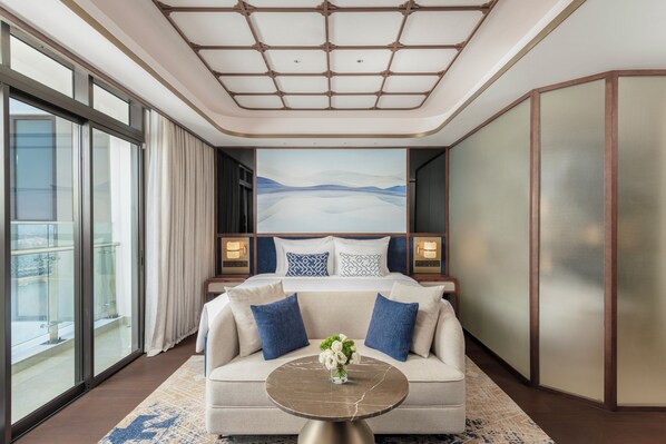 A modern hotel room with a large bed, a sofa, a round table, and a cityscape view.