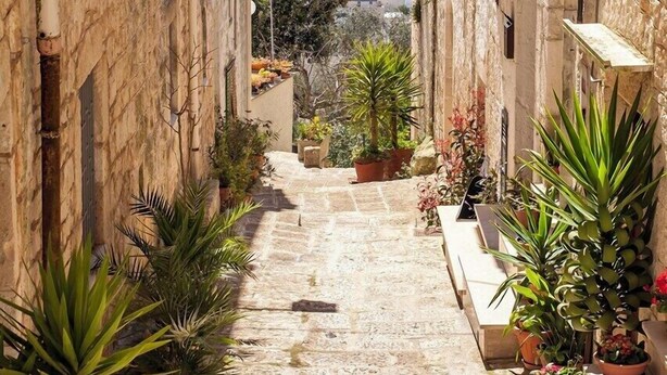 A narrow stone pathway flanked by buildings with balconies, leading to a scenic view of a valley. - Villa Eterea - Five Bedroom Villa, Sleeps 10 (Selva di Fasano)