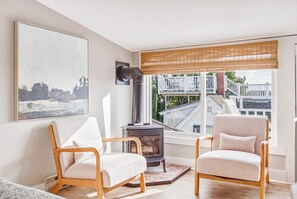Ein Wohnzimmer mit zwei Sesseln, einem Kamin, einem großen Fenster mit Blick auf Gebäude und einem Bild an der Wand.