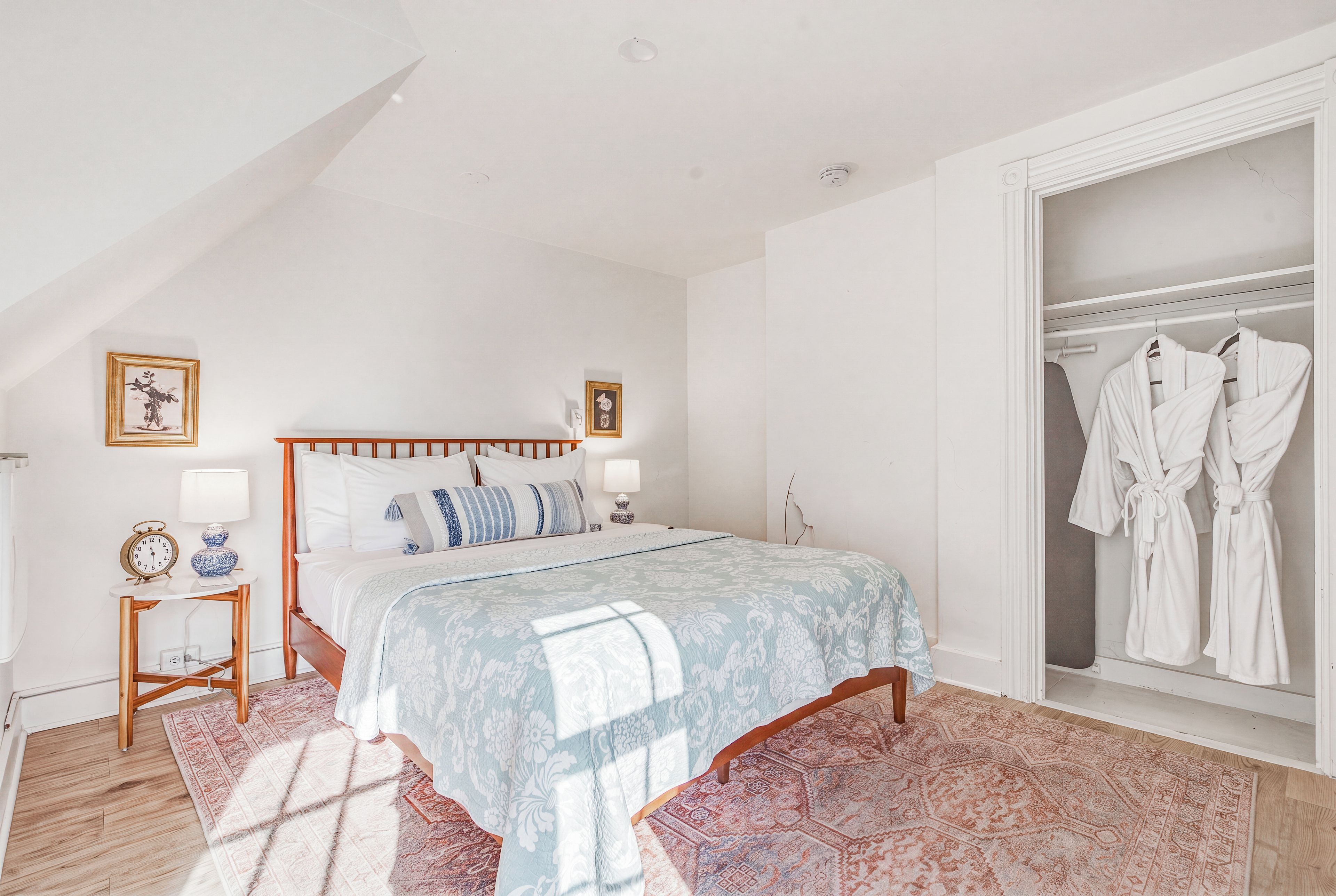 A bedroom with a bed, bedside tables, a nightstand, a wardrobe, and a hanging robe rack.