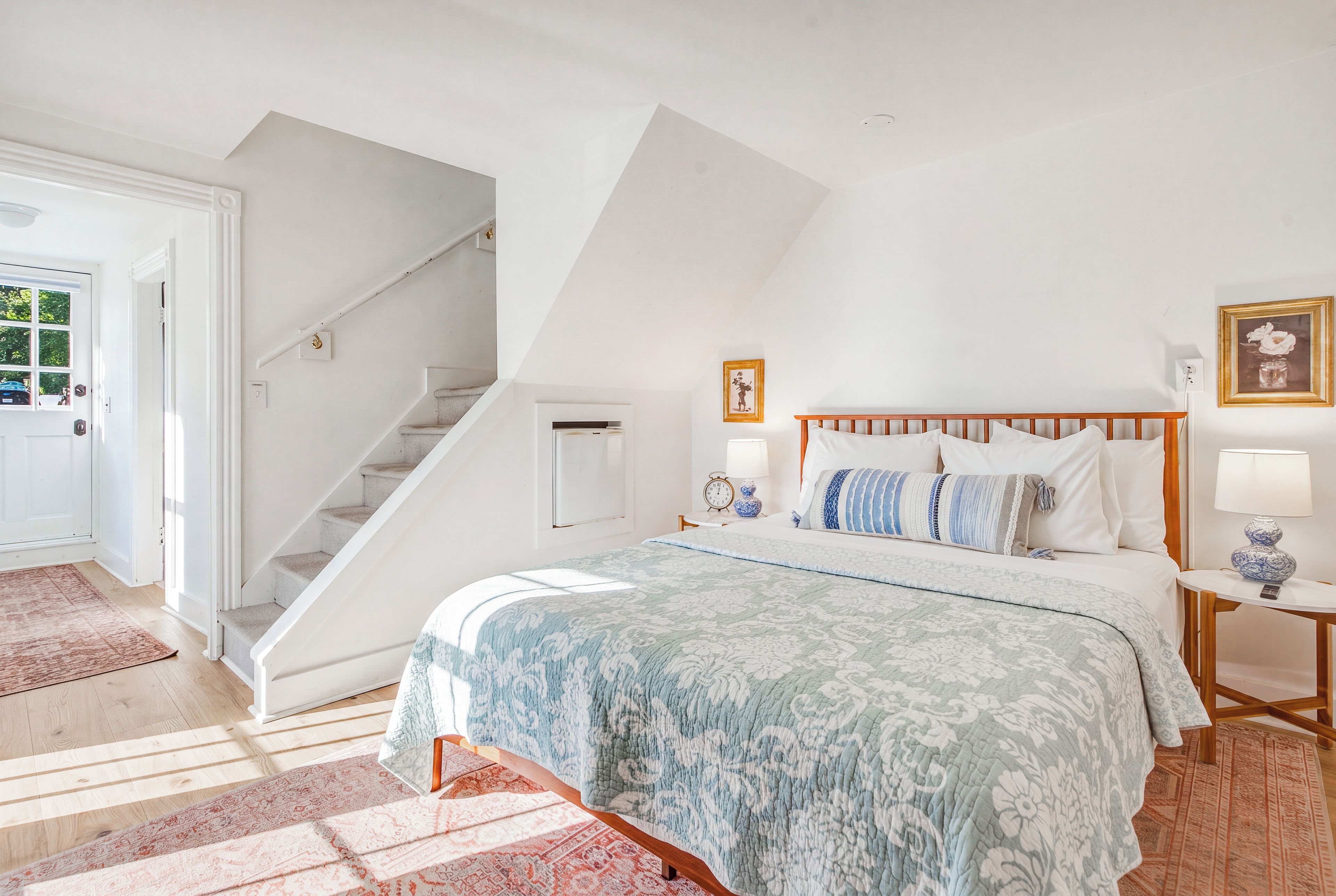 A bedroom with a bed, a nightstand, a lamp, a framed picture, and a staircase.