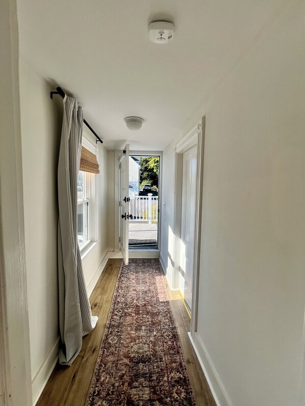 A hallway with a patterned rug, white walls, and a door leading outside. - Boothbay Harbor 2-Story Suite - Room 12 at AQ Inn - Balconies, Harbor View (Boothbay Harbor)