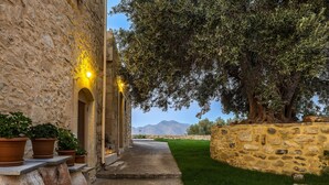 A stone pathway leading to a building with terracotta pots and a large tree providing shade. - Laga 1577 Traditional Stonehouse, a cozy retreat (Laga)
