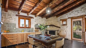A rustic kitchen with stone walls, wooden beams, and a glass-top dining table with woven chairs. - Laga 1577 Traditional Stonehouse, a cozy retreat (Laga)