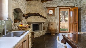 A rustic kitchen with a stone wall, wooden beams, a large ceramic pot, and a wooden door. - Laga 1577 Traditional Stonehouse, a cozy retreat (Laga)