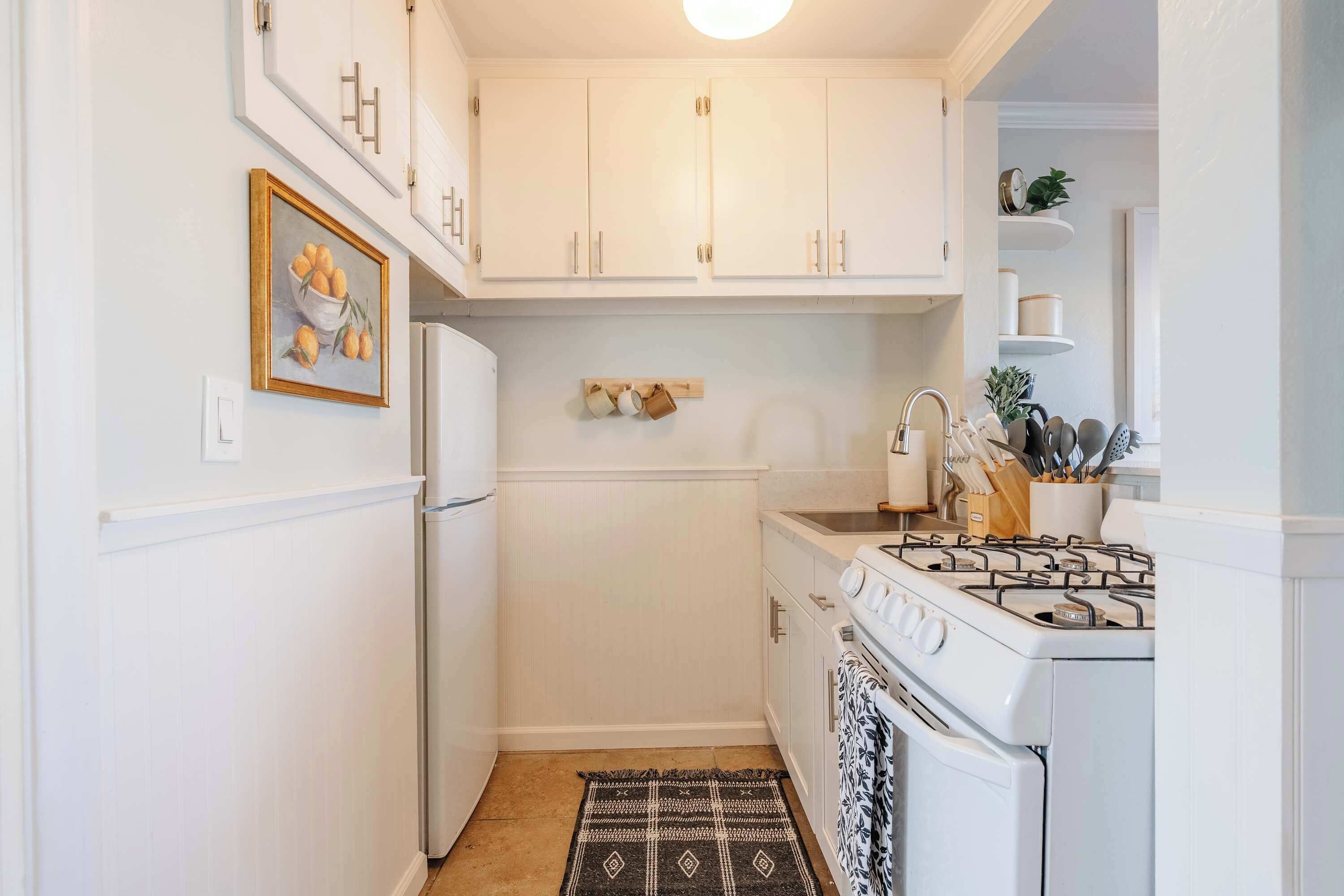 A compact kitchen with white cabinetry, a stove, and a refrigerator.