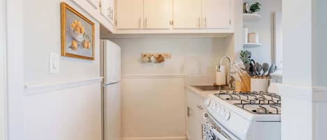 A compact kitchen with white cabinetry, a stove, and a refrigerator.