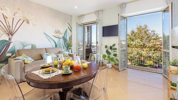 Ein modernes Wohnzimmer mit einem runden Esstisch, gedeckt für das Frühstück, einer Couch und einem Balkon mit Blick.