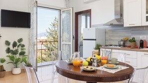 Eine moderne Küche mit Essbereich, einem an der Wand befestigten Fernseher und einem Balkon mit Pflanzen.