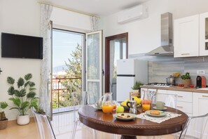 A modern kitchen with a dining area, a TV mounted on the wall, and a balcony with plants. - Chlorèa Sorrento Panoramic Apartment (Sorrento)
