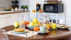 Ein Frühstückstisch mit einem Saftkrug, einem Orangensaftglas, einer Platte mit Croissants, einer Platte mit Toast und Marmelade sowie einer Schale mit Zitronen und Orangen.