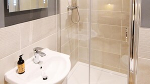 Un bany modern amb dutxa d'estuc de vidre, un rentapeus blanc i un mirall amb il·luminació.