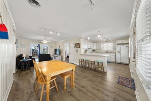 Un'ampia zona giorno con tavolo da pranzo in legno, una cucina con mobili bianchi e un angolo bar con sgabelli.