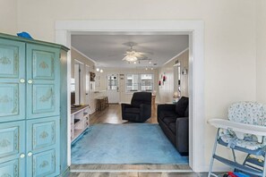 Un'ampia zona giorno con un tappeto blu, una ventola a soffitto, una poltrona nera, un'alzatavola bianco e un mobiletti color azzurro.