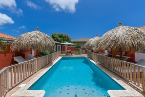 Une piscine entourée d’une terrasse en bois, de chaises longues et de parasols en chaume.