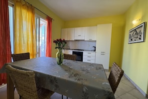 Un comedor con una mesa dispuesta para cuatro personas, rodeada de sillas de mimbre. Un jarrón con flores está sobre la mesa.