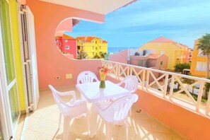 A balcony with a table and chairs, a white railing, and a view of colorful buildings. - Holiday properties Prestige Sea View (Ilha do Sal, Cape Verde)