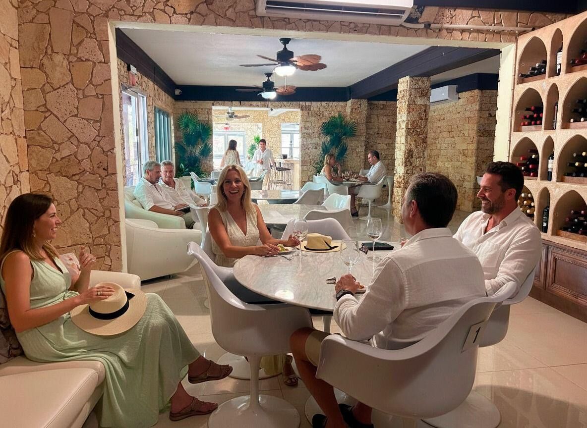 A group of people seated around a round table in a room with stone walls and a wine rack.