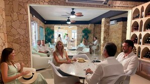 A group of people seated around a round table in a room with stone walls and a wine rack.
