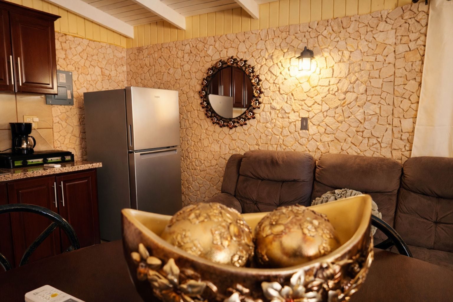 A kitchen with a stone wall, a refrigerator, a coffee maker, and a bowl of decorative items.