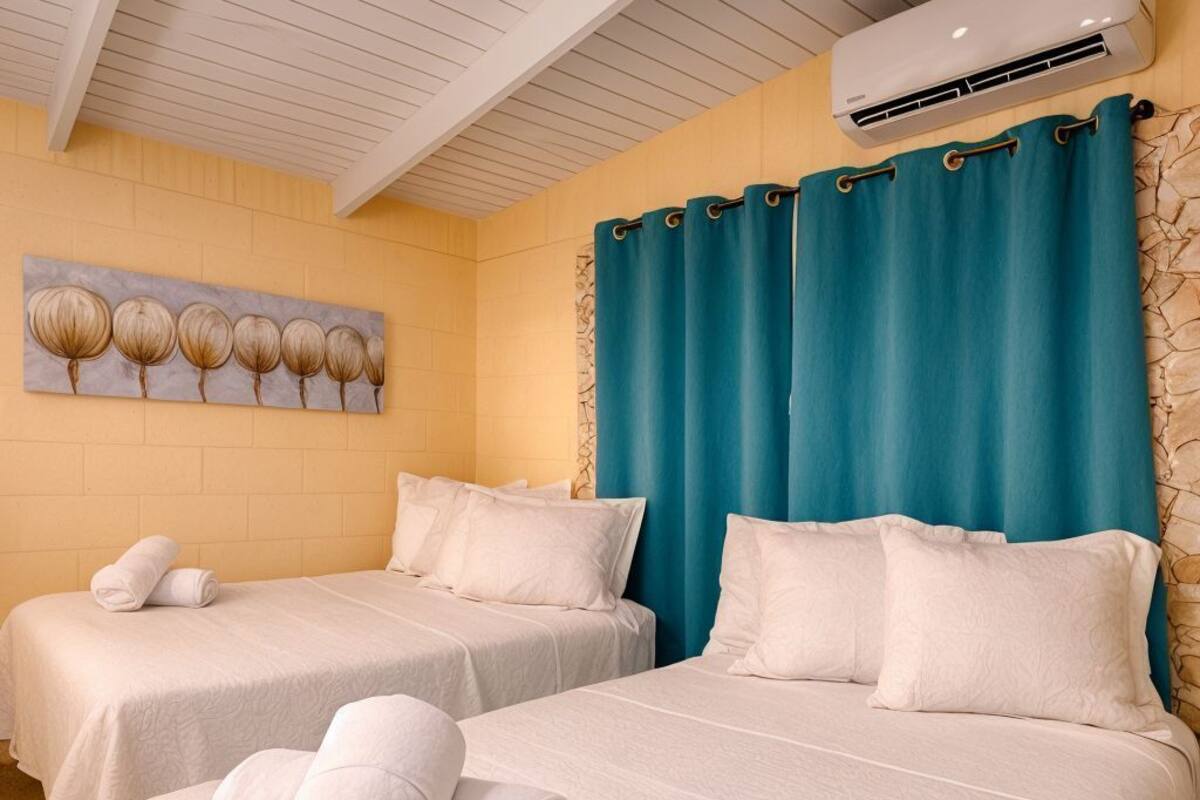 A hotel room with two beds, a ceiling fan, an air conditioning unit, and a painting on the wall.