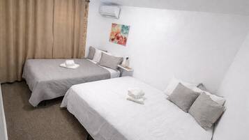 Ein Hotelzimmer mit zwei Einzelbetten, beigen Vorhängen, einem Bild an der Wand und einer Klimaanlage.