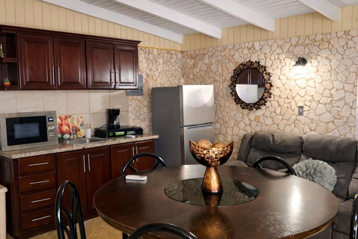 A dining area with a round table, chairs, a stone wall, a microwave, and cabinets.