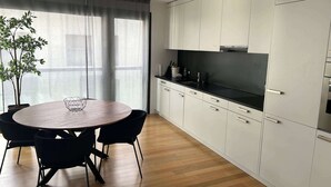 A modern kitchen with white cabinets, a black countertop, and a round dining table with chairs. - Stylish 2.5-Room + Basel Card | 6th-Floor Comfort (Basel)