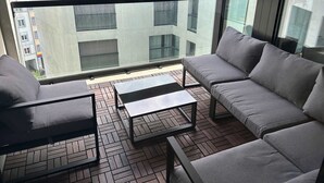 A balcony with grey sofas and a small table, overlooking a cityscape with buildings and a clear sky. - Stylish 2.5-Room + Basel Card | 6th-Floor Comfort (Basel)